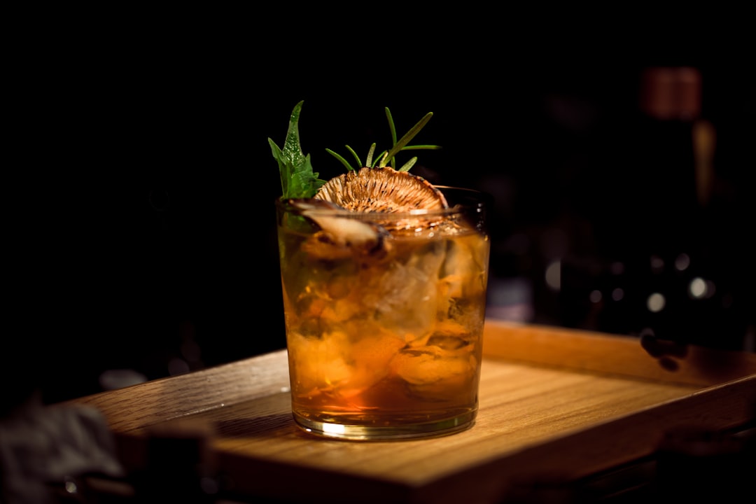 Close up of a classic Old Fashioned cocktail with an orange slice and cherry garnish on a wooden bar top
