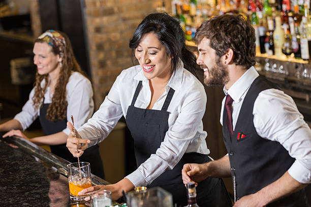A team of professional bartenders smiling confidently behind a well-stocked bar